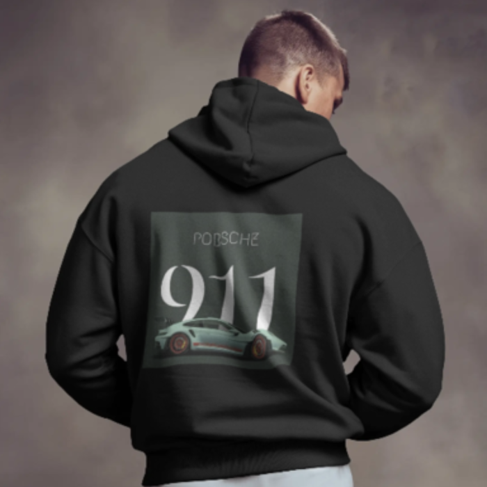 A man wearing a black hoodie with a large graphic on the back featuring a Porsche 911 car, the number “911” in metallic-style font, and the word “Porsche” above it. The background is smoky and dramatic, complementing the sleek automotive aesthetic.
