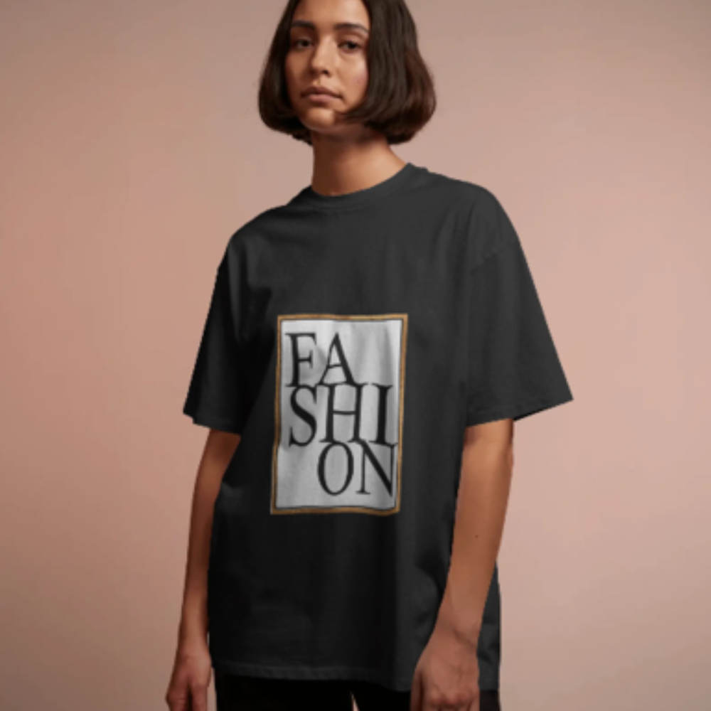 A woman with a straight bob haircut wearing a black oversized T-shirt with a large graphic text that reads “Glam Life ” in a tall serif font, arranged vertically within a gold-outlined box. The background is a soft blush pink.