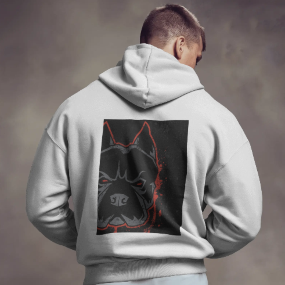 A man wearing a light gray hoodie with a striking back graphic of an intimidating dog face outlined in red, set against a dark rectangular background.