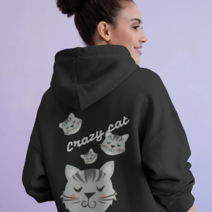 A woman wearing a black hoodie with multiple illustrated grey Crazy Cat and the phrase “Crazy Cat” in playful script printed across the back. The Merekapde hoodie has a cute and quirky aesthetic, with a soft lavender background.