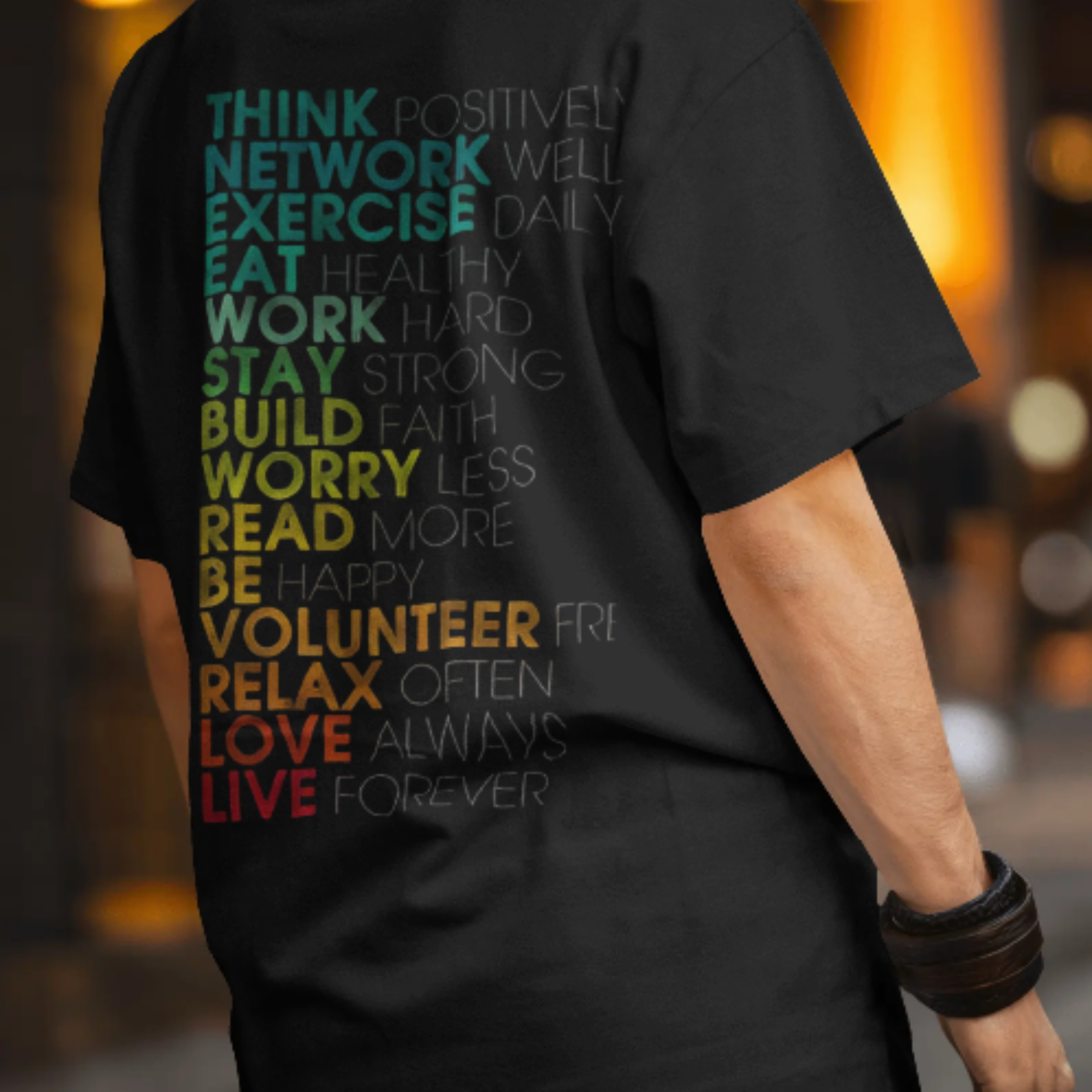 A person wearing a black T-shirt with a colorful motivational word list on the back. The words are action-driven, like “THINK Positively,” “WORK Hard,” “READ More,” and “LOVE Always,” in a rainbow of bold, merekapda gradient tones.