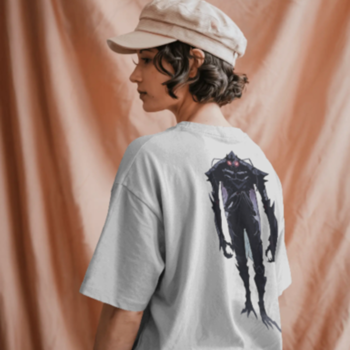 A woman wearing a light grey oversized T-shirt with a graphic of Solo Leveling a tall, dark, humanoid shadow creature with glowing red eyes printed on the back. She’s facing sideways with a neutral background draped in soft peach fabric.